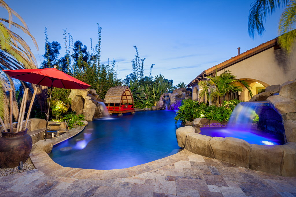 Custom Bali-style outdoor pool with multiple waterfalls, in-pool lighting, spa, cave, Balinese pavilion and tropical landscaping.
